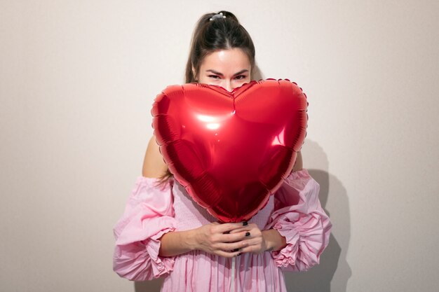 Beautiful woman celebrating valentines day in a pink dress with balloons