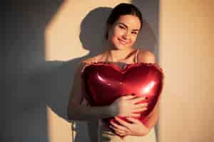 Free photo beautiful woman celebrating valentines day while holding a red heart-shaped balloon