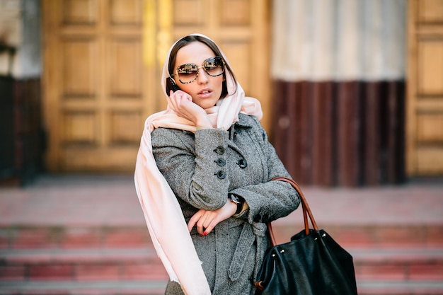 Beautiful woman in coat speaks by phone on the street