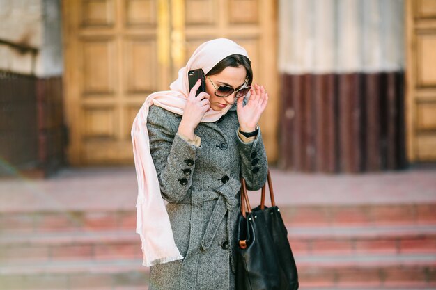 Beautiful woman in coat speaks by phone on the street