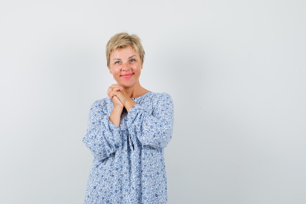 Beautiful woman combining her hands in patterned blouse and looking positive. front view.