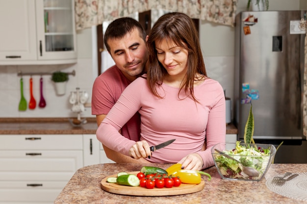 Красивая женщина режет овощи в объятиях своего парня