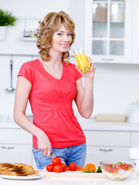 Beautiful woman drinking orange juice and cooking in the kitchen - indoors