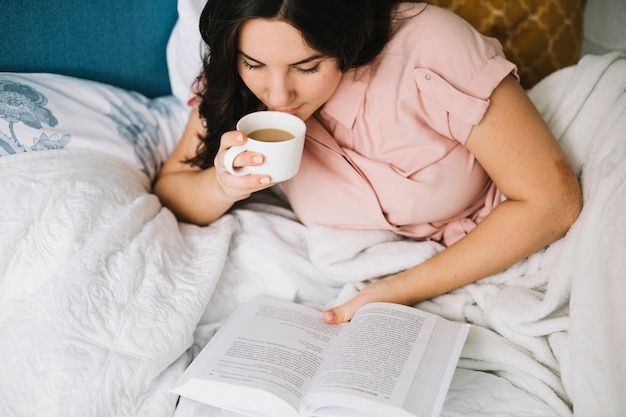 Beautiful woman drinking and reading in bed