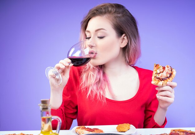 Красивая женщина пьет вино и держит в руке кусок пиццы