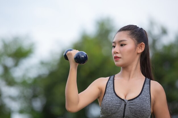 Beautiful woman exercising upper arm by lifting dumbbells on the park.