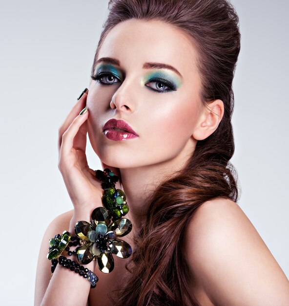 Лицо красивой женщины с модным зеленым макияжем и украшениями под рукой