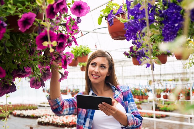 Красивая женщина-флорист с помощью планшетного компьютера в оранжерее садового центра проверяет продажу цветов