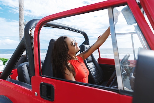 Beautiful woman going to the beach in swimming suit, sitting in car and taking selfie on sunny day near sea.