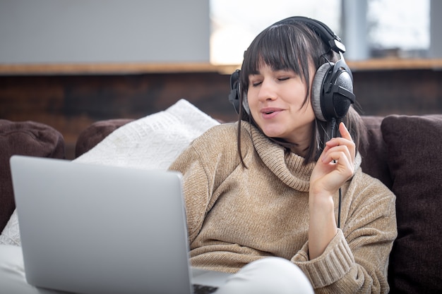 Beautiful woman in headphones listening to music at home on the couch with a laptop.