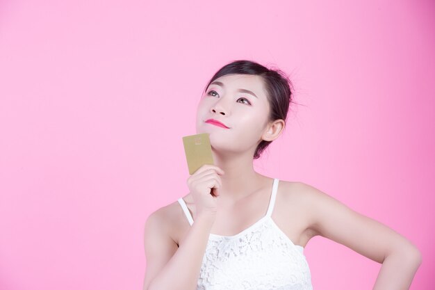 Beautiful woman holding a card on a pink background.
