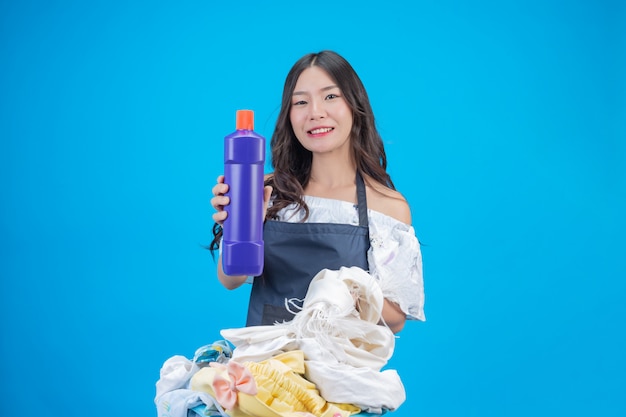 Красивая женщина, держащая ткань и жидкое моющее средство, подготовленные для стирки на синем