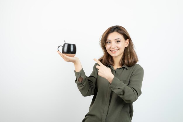 Beautiful woman holding cup of coffee and pointing at it. High quality photo