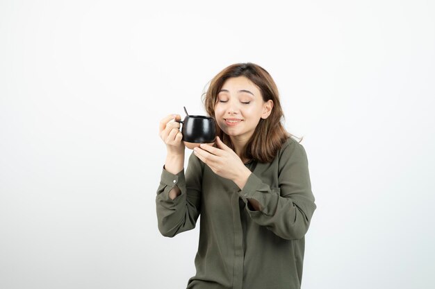 Beautiful woman holding cup of coffee and standing over white. High quality photo