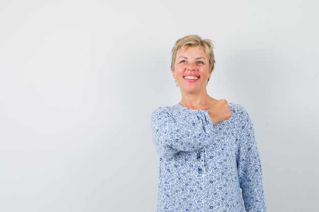 Beautiful woman holding fist on her chest in patterned blouse and looking proudly , front view. space for text