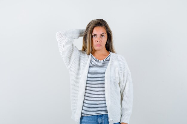 Beautiful woman holding hand behind head in jacket and looking thoughtful , front view.