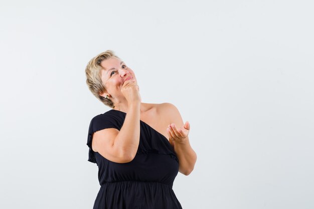 Beautiful woman holding hand on mouth while looking up in black blouse and looking thoughtful