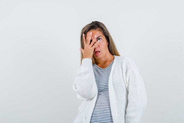 Beautiful woman holding hand near face in jacket and looking puzzled , front view.