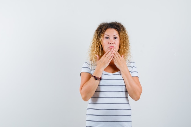 Beautiful woman holding hands on chin in t-shirt and looking surprised , front view.