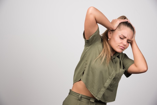 Beautiful woman holding her head on gray wall.