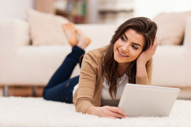 Beautiful woman holding her tablet while lying down on carpet