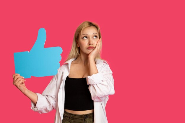 ピンクの背景に孤立したライクボタンを握っている美しい女性