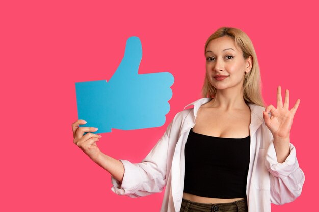 Beautiful woman holding a like button isolated on pink background
