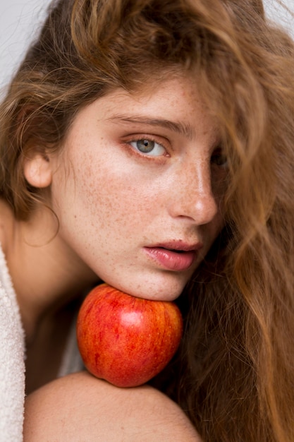 Beautiful woman holding a red apple between her face and knee