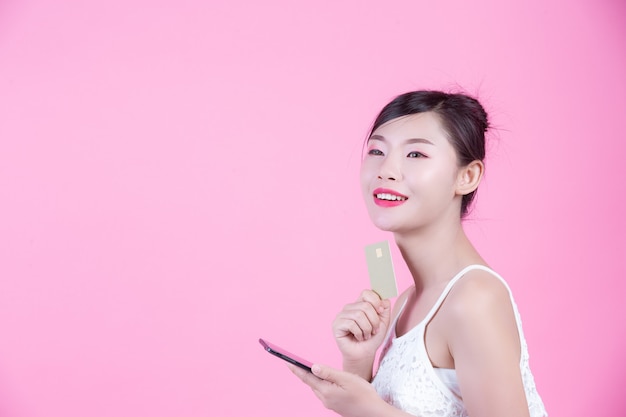 Beautiful woman holding a smartphone and card on a pink background