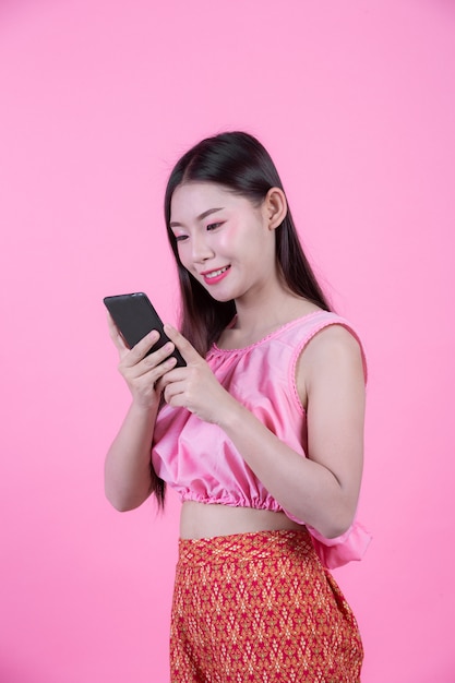 Beautiful woman holding a smartphone on a pink background.