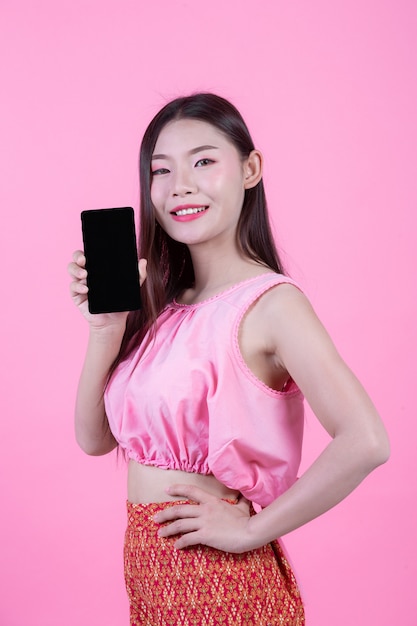 Beautiful woman holding a smartphone on a pink background.