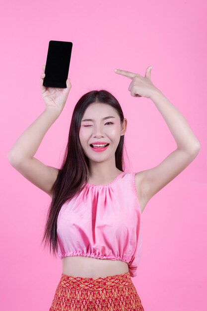 Beautiful woman holding a smartphone on a pink background.