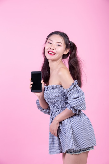 Beautiful woman holding a smartphone on a pink background.