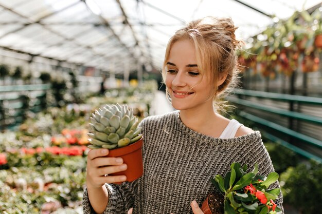 Beautiful woman holding succulent and pink flower. Snapshot of woman in knitted outfit.