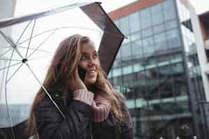 Free photo beautiful woman holding an umbrella and talking on mobile phone