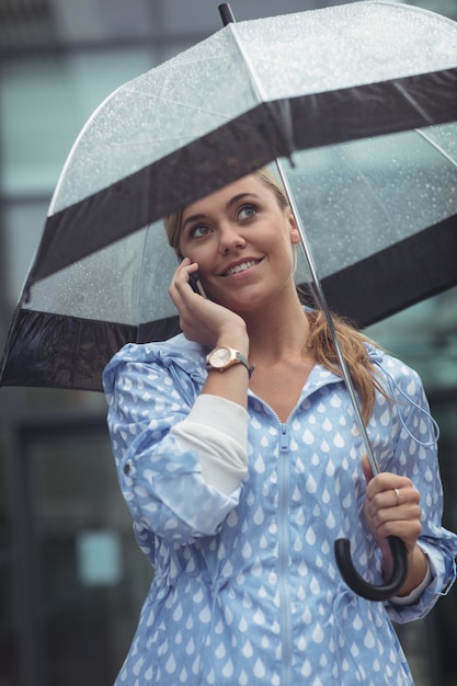Beautiful woman holding umbrella while talking on mobile phone