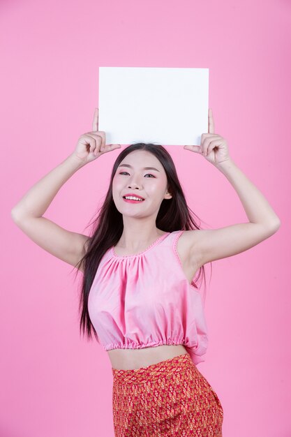 Beautiful woman holding a white board sheet on a pink background.