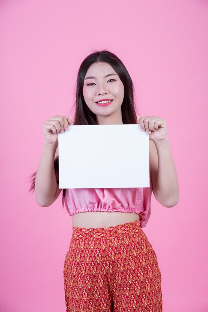 Beautiful woman holding a white board sheet on a pink background.