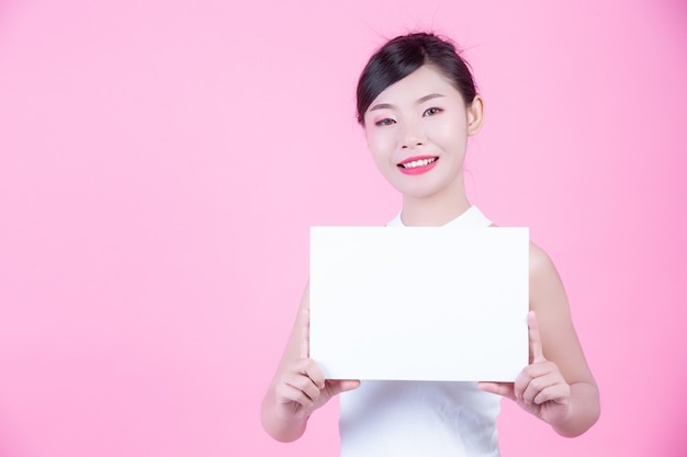 Beautiful woman holding a white board sheet on a pink background.