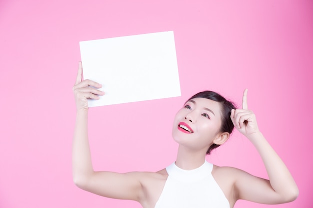 Beautiful woman holding a white board sheet on a pink background.