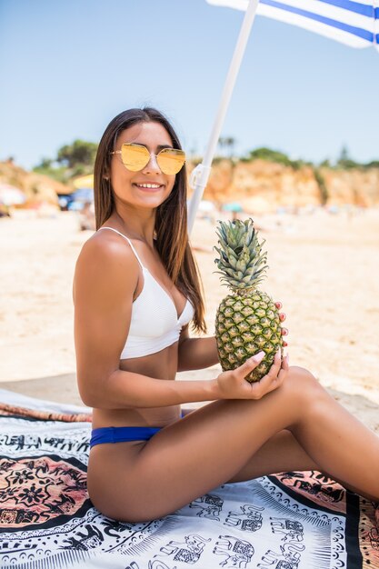 美しい女性はビーチでパイナップルフルーツを保持しています。