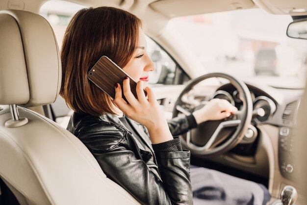 美しい女性が携帯電話で話していて、車に座っている間に笑っている