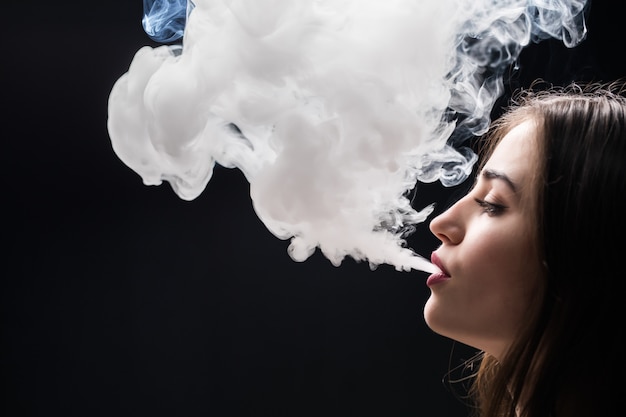 Beautiful woman is vaping isolated on black wall