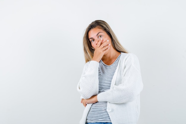 Beautiful woman in jacket covering mouth with hand and looking shocked , front view.