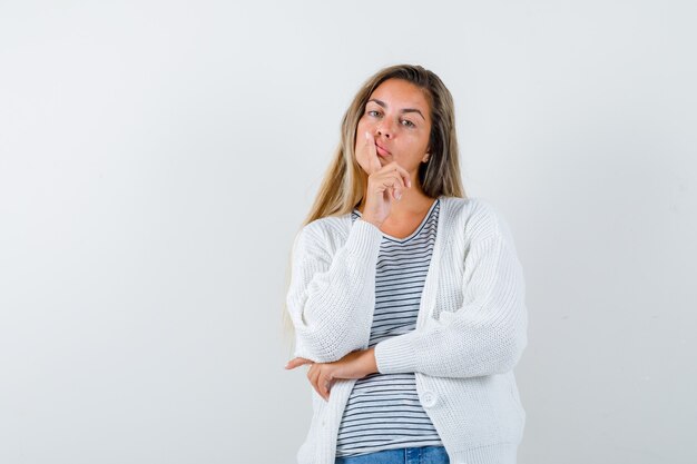 Beautiful woman in jacket holding finger on lips and looking thoughtful , front view.