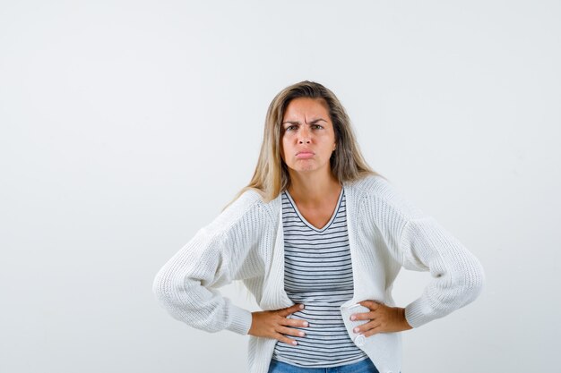 Beautiful woman in jacket holding hands on waist and looking skeptic , front view.