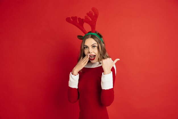 Beautiful woman like christmas deer isolated on red wall concept 
