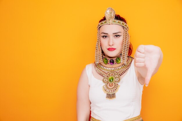 Красивая женщина, как клеопатра в древнем египетском костюме, недовольна, показывая большой палец на апельсине