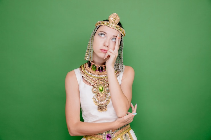 मुफ़्त फोटो beautiful woman like cleopatra in ancient egyptian costume loking up with pensive expression thinking on green