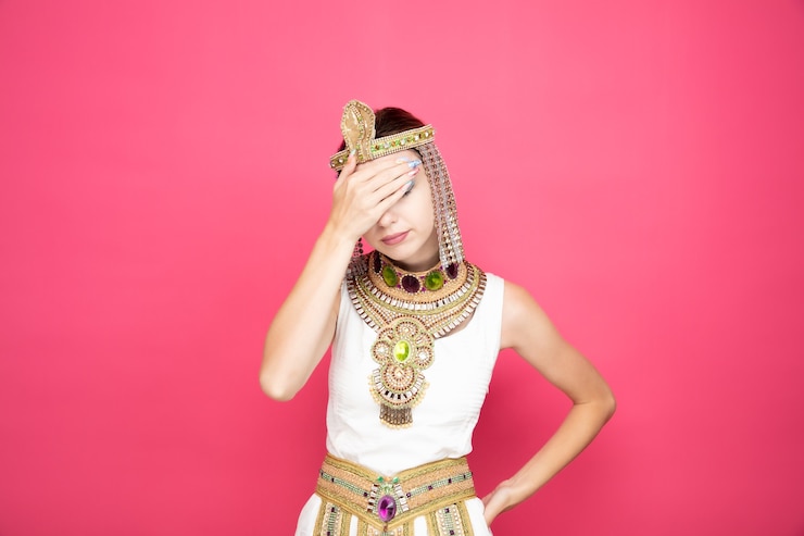 Free Photo beautiful woman like cleopatra in ancient egyptian costume looking tired and bored covering eyes with palm on pink